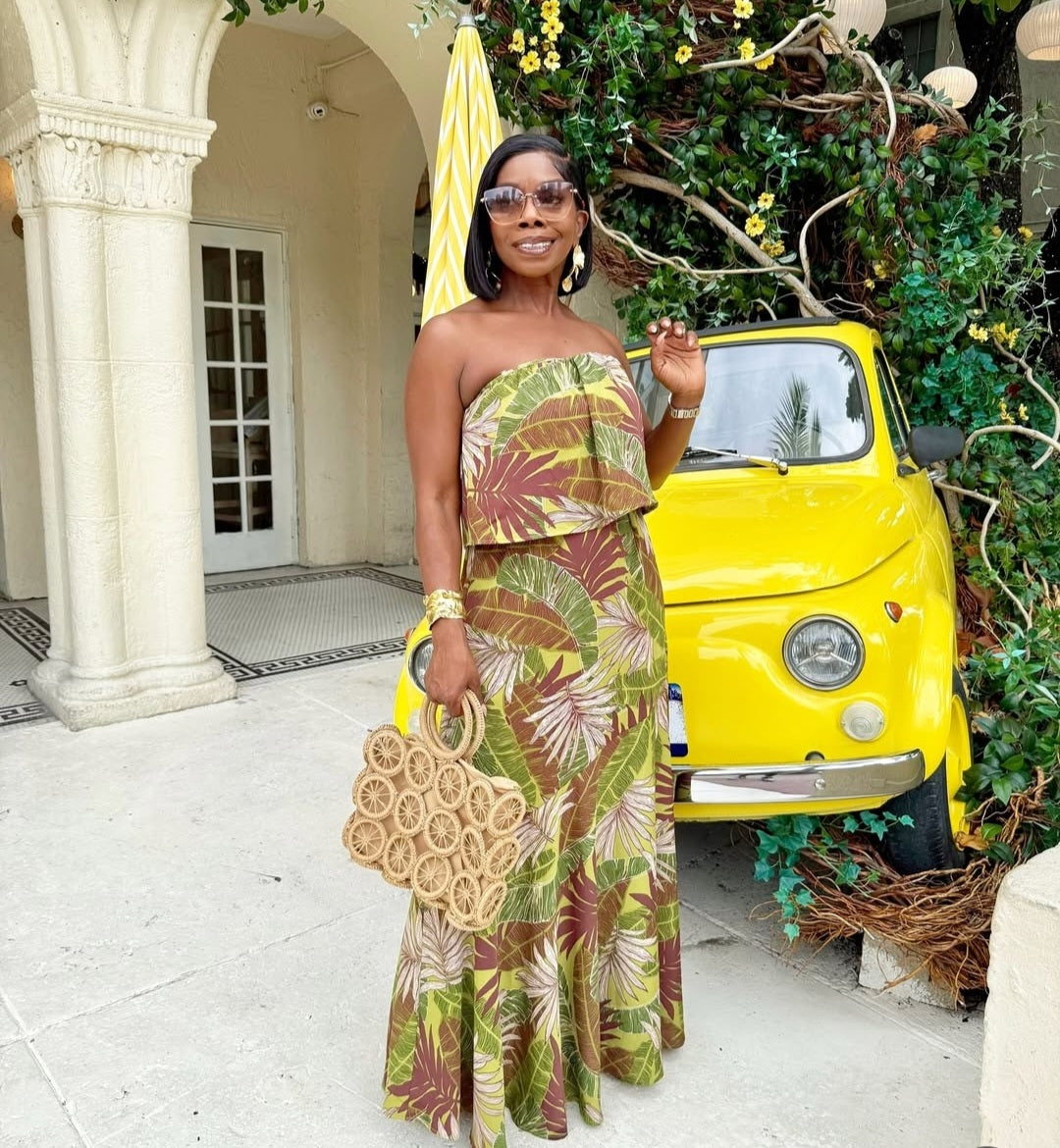 Woman in a floral dress standing next to a yellow car with decorative plants in the background