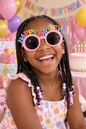 Black 8-year-old girl with braids wearing the exact pink Happy Birthday sunglasses at a party
