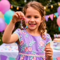 Girl smiling as she holds up and admires a pastel butterfly bead bracelet at a festive party