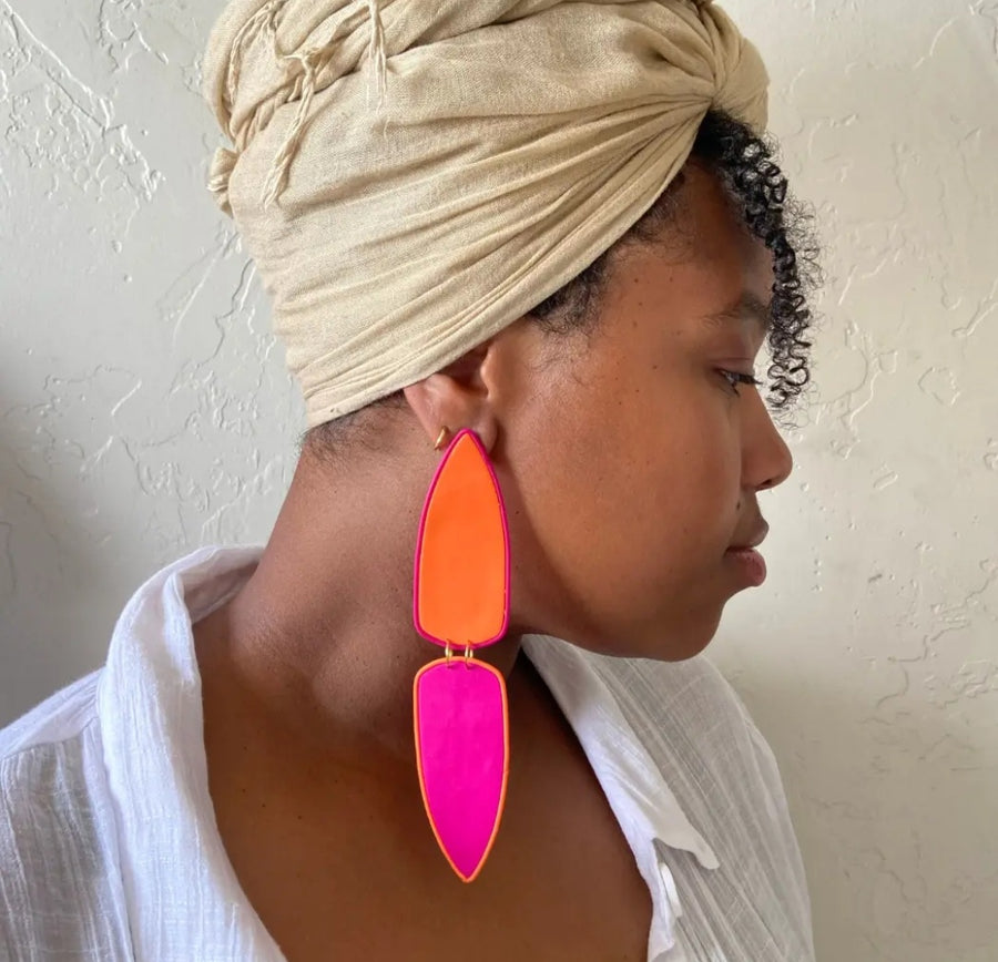 Woman wearing a beige headscarf and colorful earrings against a neutral background