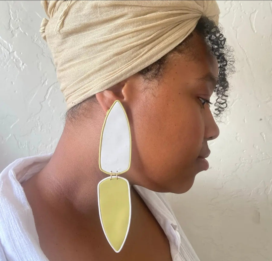 Woman wearing a beige headscarf and large green earrings against a light background